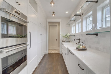 Design ideas for a small traditional galley enclosed kitchen in Minneapolis with a belfast sink, shaker cabinets, white cabinets, granite worktops, grey splashback, marble splashback, integrated appliances, dark hardwood flooring, no island, brown floors and white worktops.