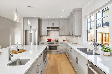 Mid-sized elegant l-shaped light wood floor eat-in kitchen photo in Vancouver with a double-bowl sink, shaker cabinets, gray cabinets, quartz countertops, white backsplash, ceramic backsplash, stainless steel appliances and an island