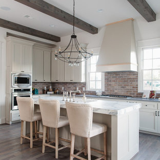 Farmhouse kitchen remodeling - Example of a farmhouse dark wood floor and brown floor kitchen design in Birmingham with shaker cabinets, white cabinets, red backsplash, brick backsplash, black appliances and an island