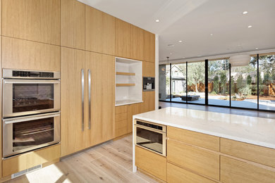 Example of a mid-sized trendy u-shaped medium tone wood floor and brown floor enclosed kitchen design in San Francisco with flat-panel cabinets, light wood cabinets, quartz countertops, paneled appliances, a peninsula and white countertops