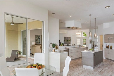 Open concept kitchen - mid-sized contemporary l-shaped porcelain tile and multicolored floor open concept kitchen idea in Tampa with a single-bowl sink, flat-panel cabinets, beige cabinets, quartz countertops, white backsplash, stone slab backsplash, stainless steel appliances and an island