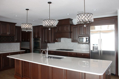 Example of a large trendy l-shaped medium tone wood floor and brown floor open concept kitchen design in Other with an undermount sink, raised-panel cabinets, dark wood cabinets, quartz countertops, gray backsplash, subway tile backsplash, stainless steel appliances and an island