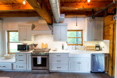 Exemple d'une cuisine américaine linéaire montagne avec un évier de ferme, un placard à porte shaker, une crédence blanche et un électroménager en acier inoxydable.