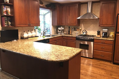 Example of a mid-sized classic u-shaped medium tone wood floor and brown floor eat-in kitchen design in San Francisco with an undermount sink, raised-panel cabinets, dark wood cabinets, granite countertops, beige backsplash, ceramic backsplash, stainless steel appliances and a peninsula