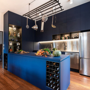 This is an example of a large contemporary u-shaped kitchen in Melbourne with a double-bowl sink, flat-panel cabinets, blue cabinets, solid surface benchtops, grey splashback, metal splashback, stainless steel appliances, medium hardwood floors, a peninsula, brown floor and blue benchtop.