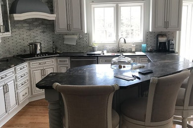 Eat-in kitchen - large traditional l-shaped light wood floor and brown floor eat-in kitchen idea in Other with an undermount sink, raised-panel cabinets, white cabinets, quartzite countertops, gray backsplash, porcelain backsplash, stainless steel appliances, an island and black countertops