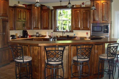 Modelo de cocina clásica grande abierta con armarios con paneles con relieve, puertas de armario de madera oscura, electrodomésticos de acero inoxidable y suelo de madera en tonos medios