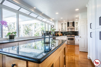 Example of a large transitional u-shaped light wood floor enclosed kitchen design in Orange County with an undermount sink, recessed-panel cabinets, white cabinets, quartz countertops, multicolored backsplash, stone slab backsplash, stainless steel appliances and an island