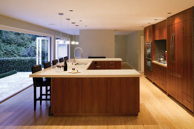 This is an example of a medium sized contemporary u-shaped enclosed kitchen in Orange County with a double-bowl sink, flat-panel cabinets, medium wood cabinets, engineered stone countertops, grey splashback, stone tiled splashback, integrated appliances, light hardwood flooring, an island and beige floors.