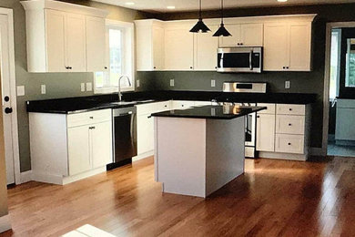 Small transitional l-shaped medium tone wood floor and brown floor eat-in kitchen photo in Boston with an undermount sink, shaker cabinets, white cabinets, granite countertops, black backsplash, granite backsplash, stainless steel appliances, an island and black countertops