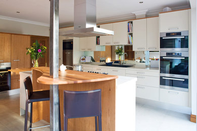 Medium sized contemporary kitchen/diner in Dublin with a double-bowl sink, flat-panel cabinets, beige cabinets, engineered stone countertops, mirror splashback, stainless steel appliances, porcelain flooring and an island.