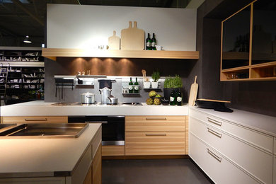 Imagen de cocinas en L contemporánea de tamaño medio abierta con armarios estilo shaker, puertas de armario de madera clara, salpicadero verde y suelo de cemento