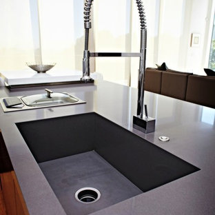 Inspiration for a large contemporary galley open plan kitchen in Seattle with an integrated sink, quartz benchtops, flat-panel cabinets, dark wood cabinets, stainless steel appliances, light hardwood floors, with island, beige floor and grey benchtop.
