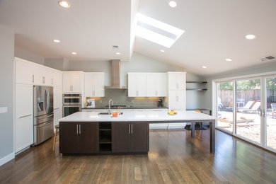 Example of a large trendy l-shaped medium tone wood floor open concept kitchen design in San Francisco with a double-bowl sink, shaker cabinets, white cabinets, quartzite countertops, gray backsplash, matchstick tile backsplash, stainless steel appliances and an island