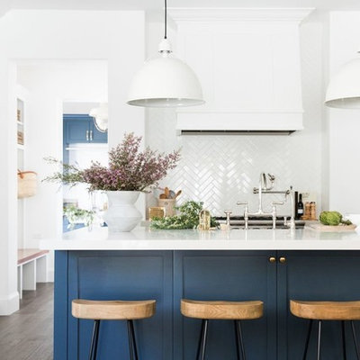 Open concept kitchen - large transitional galley dark wood floor open concept kitchen idea in Salt Lake City with a farmhouse sink, shaker cabinets, blue cabinets, white backsplash, subway tile backsplash, stainless steel appliances, an island and white countertops