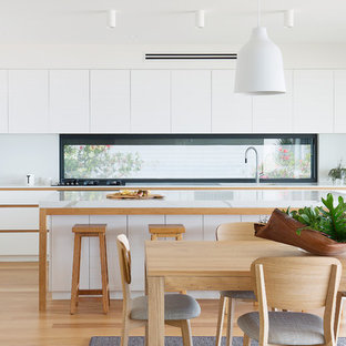 Design ideas for a contemporary l-shaped eat-in kitchen in Sydney with quartz benchtops, white benchtop, flat-panel cabinets, white cabinets, window splashback, white appliances, medium hardwood floors, with island and brown floor.