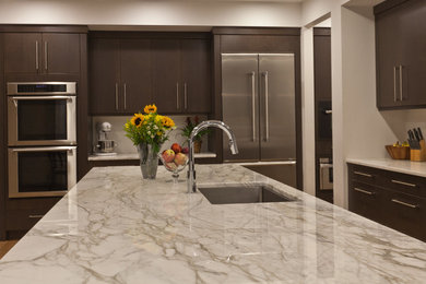 Example of a trendy light wood floor kitchen design in Raleigh with a single-bowl sink, flat-panel cabinets, dark wood cabinets, marble countertops, white backsplash, white appliances and an island
