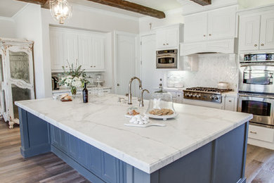 Mid-sized transitional u-shaped medium tone wood floor eat-in kitchen photo in Dallas with an undermount sink, recessed-panel cabinets, white cabinets, marble countertops, white backsplash, stone slab backsplash, stainless steel appliances and an island