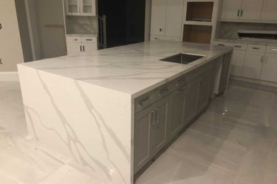 Example of a large trendy l-shaped porcelain tile and gray floor eat-in kitchen design in Miami with a triple-bowl sink, flat-panel cabinets, gray cabinets, quartz countertops, white backsplash, stone slab backsplash, stainless steel appliances, an island and white countertops