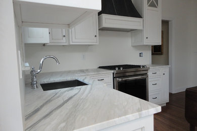 Inspiration for a mid-sized timeless l-shaped medium tone wood floor enclosed kitchen remodel in New York with an undermount sink, recessed-panel cabinets, white cabinets, marble countertops, stainless steel appliances and an island