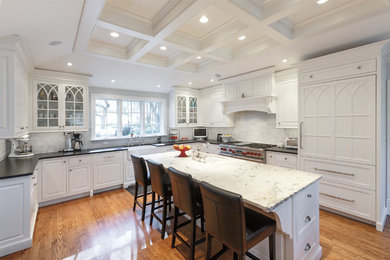 Example of a large trendy u-shaped medium tone wood floor and brown floor enclosed kitchen design in Philadelphia with a farmhouse sink, louvered cabinets, white cabinets, marble countertops, gray backsplash, marble backsplash, stainless steel appliances and an island