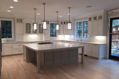 This is an example of a medium sized contemporary u-shaped kitchen in DC Metro with shaker cabinets, composite countertops, an island, a submerged sink, white cabinets, white splashback, porcelain splashback, stainless steel appliances, light hardwood flooring and brown floors.