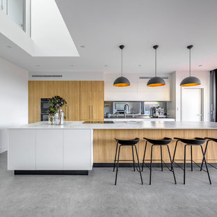 Contemporary galley open plan kitchen in Sydney with flat-panel cabinets, light wood cabinets, metallic splashback, mirror splashback, panelled appliances, with island, grey floor and white benchtop.
