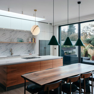 This is an example of a medium sized modern galley kitchen/diner in Gloucestershire with flat-panel cabinets, yellow cabinets, white splashback, marble splashback, an island, brown floors, a double-bowl sink, stainless steel appliances and light hardwood flooring.