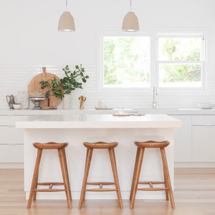 Contemporary l-shaped kitchen in Geelong with an undermount sink, flat-panel cabinets, white cabinets, white splashback, stainless steel appliances, light hardwood floors, with island, beige floor and white benchtop.
