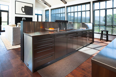 Example of a large trendy galley medium tone wood floor and brown floor kitchen design in San Francisco with an integrated sink, flat-panel cabinets, stainless steel cabinets, stainless steel countertops, black backsplash, stainless steel appliances and two islands