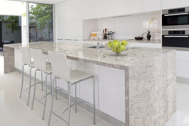 Inspiration for a mid-sized modern galley open concept kitchen remodel in San Diego with flat-panel cabinets, white cabinets, quartz countertops, white backsplash, white appliances and an island