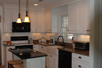 Example of a mid-sized classic u-shaped ceramic tile and beige floor eat-in kitchen design in Other with a farmhouse sink, white cabinets, white backsplash, black appliances, an island, raised-panel cabinets and solid surface countertops