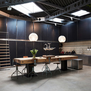 This is an example of an expansive industrial single-wall kitchen/diner in London with flat-panel cabinets, black cabinets, stainless steel appliances, concrete flooring, grey floors, a built-in sink, stainless steel worktops and brown splashback.