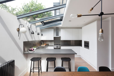 Mittelgroße Moderne Küche in U-Form mit flächenbündigen Schrankfronten, weißen Schränken, Küchenrückwand in Metallic und Halbinsel in London