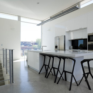 Photo of a contemporary galley kitchen in Perth with flat-panel cabinets, white cabinets, black splashback, glass sheet splashback, stainless steel appliances, terrazzo floors, with island and grey floor.