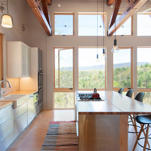 Photo of a modern eat-in kitchen with a farmhouse sink, stainless steel cabinets, wood benchtops, stainless steel appliances, plywood floors, with island and exposed beam.