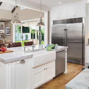 Large transitional u-shaped separate kitchen in Phoenix with a farmhouse sink, shaker cabinets, white cabinets, onyx benchtops, white splashback, ceramic splashback, stainless steel appliances, light hardwood floors, with island and brown floor.