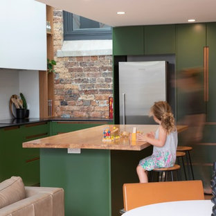 Design ideas for a contemporary l-shaped open plan kitchen in Sydney with an undermount sink, flat-panel cabinets, green cabinets, white splashback, stainless steel appliances, medium hardwood floors, with island, brown floor and black benchtop.