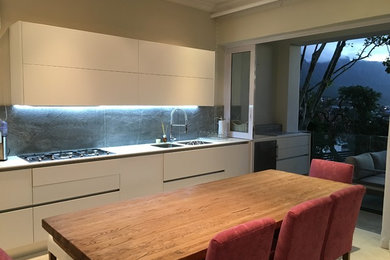 Immagine di una cucina minimal di medie dimensioni con ante lisce, ante bianche, paraspruzzi grigio, paraspruzzi in lastra di pietra, elettrodomestici in acciaio inossidabile e nessuna isola