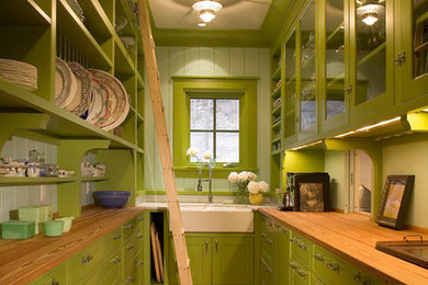 Inspiration for a country u-shaped medium tone wood floor kitchen pantry remodel in Minneapolis with a farmhouse sink, glass-front cabinets, green cabinets, wood countertops, green backsplash, glass tile backsplash and no island