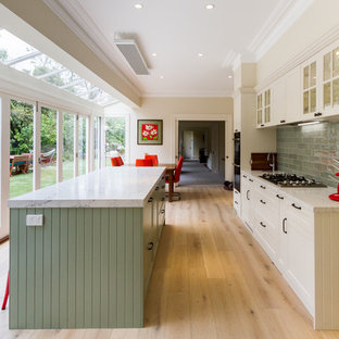 Design ideas for a mid-sized transitional galley eat-in kitchen in Melbourne with shaker cabinets, white cabinets, quartz benchtops, green splashback, subway tile splashback, black appliances, light hardwood floors, with island, beige floor and white benchtop.
