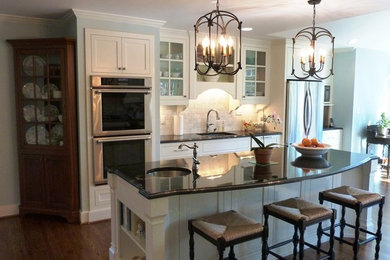 Inspiration for a mid-sized timeless u-shaped medium tone wood floor eat-in kitchen remodel in Raleigh with an undermount sink, recessed-panel cabinets, white cabinets, granite countertops, gray backsplash, stone tile backsplash, stainless steel appliances and an island