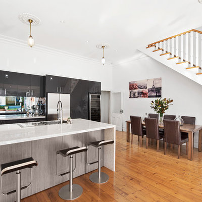 Trendy u-shaped light wood floor open concept kitchen photo in Melbourne with a drop-in sink, flat-panel cabinets, black cabinets, glass sheet backsplash, stainless steel appliances and a peninsula