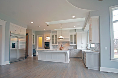 Inspiration for a mid-sized transitional u-shaped medium tone wood floor and gray floor open concept kitchen remodel in Cleveland with a farmhouse sink, recessed-panel cabinets, gray cabinets, granite countertops, gray backsplash, ceramic backsplash, stainless steel appliances and an island