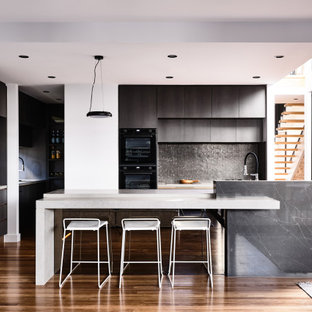 Photo of a contemporary u-shaped open plan kitchen in Brisbane with flat-panel cabinets, black cabinets, black splashback, mosaic tile splashback, black appliances, medium hardwood floors, with island, brown floor and white benchtop.