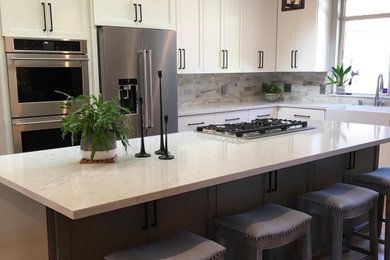 Transitional l-shaped medium tone wood floor kitchen photo in Other with a farmhouse sink, shaker cabinets, white cabinets, quartz countertops, porcelain backsplash, stainless steel appliances and an island