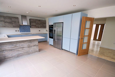 Design ideas for a medium sized contemporary u-shaped kitchen/diner in Buckinghamshire with a submerged sink, flat-panel cabinets, blue cabinets, engineered stone countertops, blue splashback, metro tiled splashback, stainless steel appliances, ceramic flooring, a breakfast bar, brown floors and white worktops.