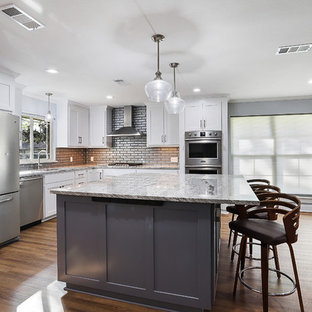 Large transitional open concept kitchen photos - Example of a large transitional u-shaped vinyl floor and brown floor open concept kitchen design in New Orleans with a single-bowl sink, shaker cabinets, white cabinets, granite countertops, gray backsplash, glass tile backsplash, stainless steel appliances, an island and white countertops