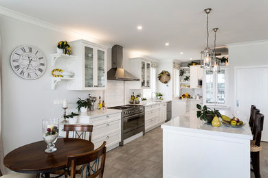 This is an example of a large traditional galley kitchen/diner in Auckland with a submerged sink, recessed-panel cabinets, white cabinets, engineered stone countertops, white splashback, porcelain splashback, stainless steel appliances, medium hardwood flooring, an island and brown floors.