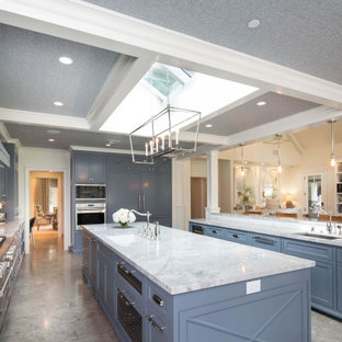 Idée de décoration pour une très grand cuisine américaine tradition en L avec un évier encastré, un placard à porte shaker, des portes de placard bleues, un plan de travail en quartz, une crédence blanche, une crédence en carreau de céramique, un électroménager encastrable, un sol en calcaire, 2 îlots, un sol gris et un plan de travail blanc.